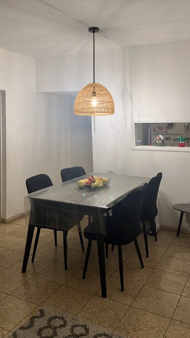 אחרי: מנורת תלייה מראטן טבעי מעל שולחן האוכל, דולקת