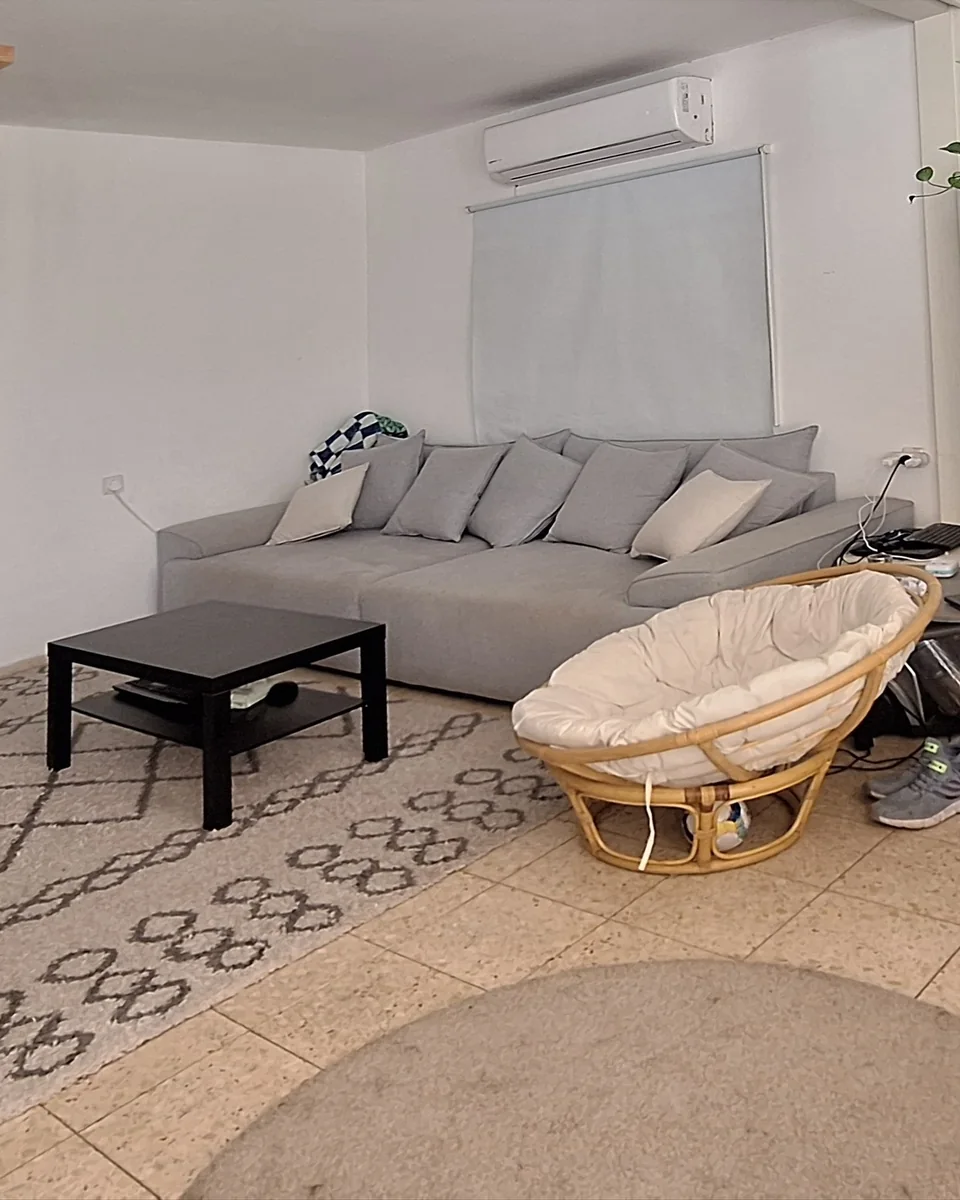 לפני: סלון עם ספה אפורה, שולחן סלון שחור וכיסא ראטן עגול, בלי המנורות